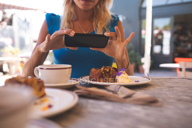 Средняя секция женщины фотографирует с мобильного телефона в кафе на открытом воздухе — стоковое фото