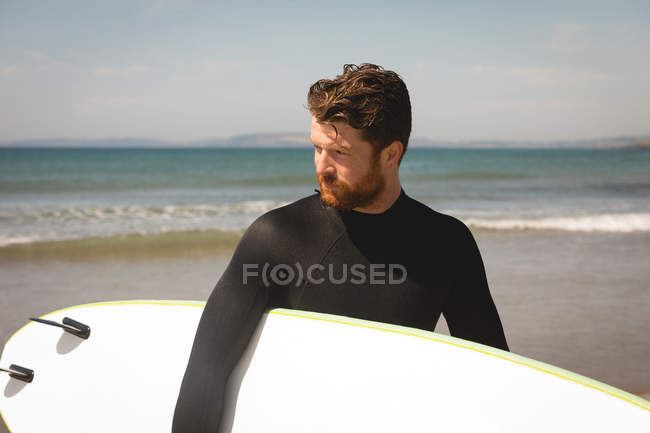 Surfista com prancha andando na praia em um dia ensolarado — Fotografia de Stock
