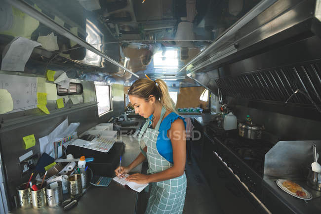 Woman waitress writing orders on notepad in food truck — Stock Photo