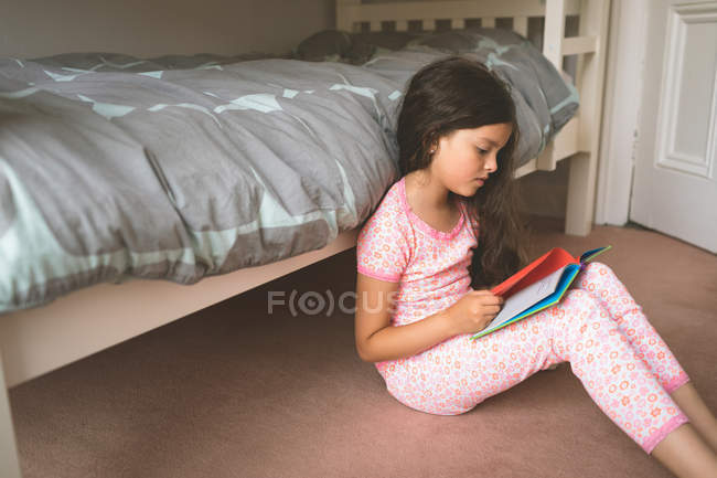 Chica leyendo libro en el dormitorio en casa - foto de stock