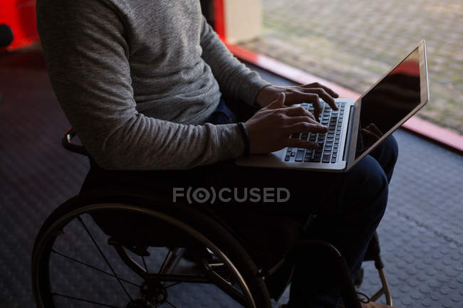 Sección media del hombre discapacitado usando el ordenador portátil en el taller - foto de stock