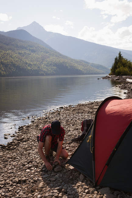 Человек расставляет палатку у реки в горах — стоковое фото