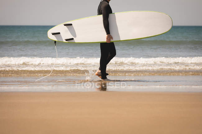 Низкая часть серфера с доской для серфинга, прогуливающегося по пляжу — стоковое фото