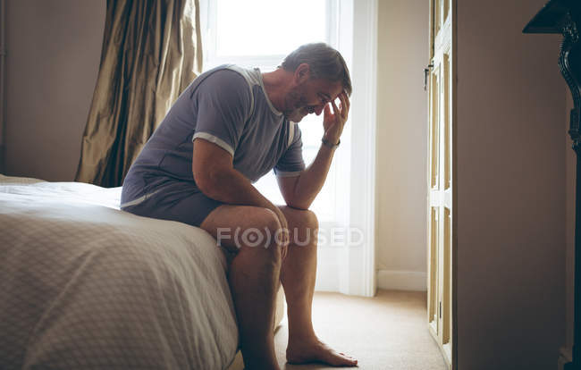 Homme âgé tendu assis sur le lit dans la chambre à coucher à la maison — Photo de stock