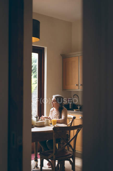 Femme âgée prenant le petit déjeuner sur la table à manger à la maison — Photo de stock