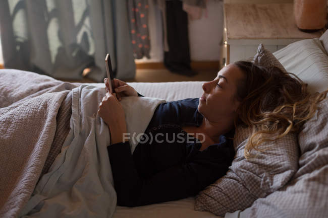 Femme utilisant un téléphone portable sur le lit à la maison — Photo de stock