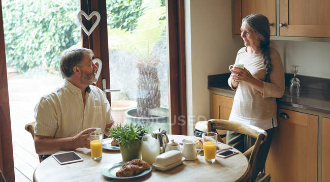 Senior couple interacting with each other while having breakfast at home — Stock Photo
