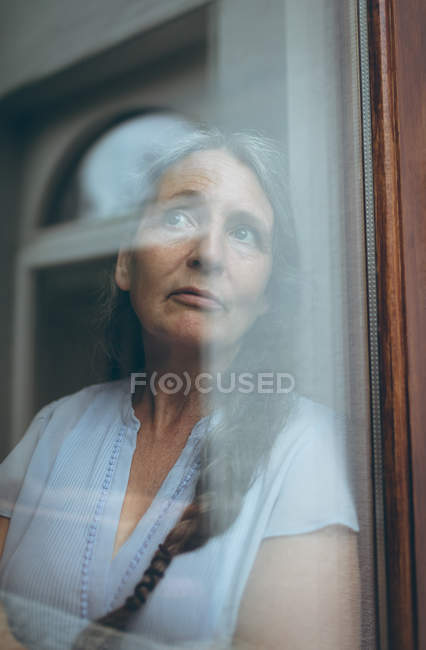 Ragionevole donna anziana guardando attraverso la finestra a casa — Foto stock