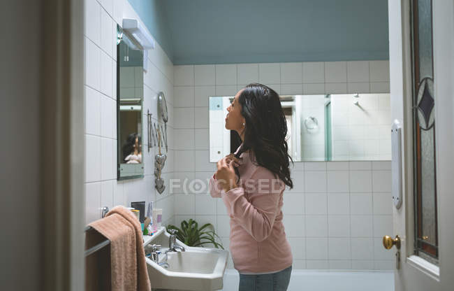 Женщина расчесывает волосы перед зеркалом ванной комнаты дома — стоковое фото