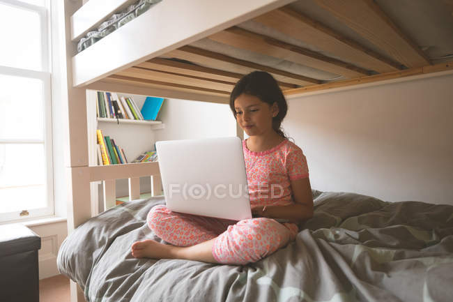 Chica joven usando el ordenador portátil en la cama en el dormitorio en casa - foto de stock