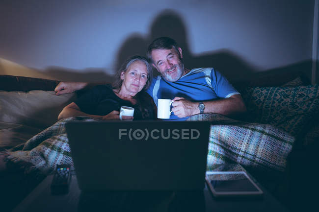 Feliz pareja de ancianos viendo el ordenador portátil mientras toma café en casa - foto de stock