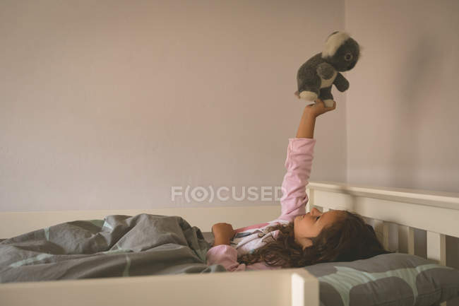 Girl playing with teddy bear on bed at home — Stock Photo