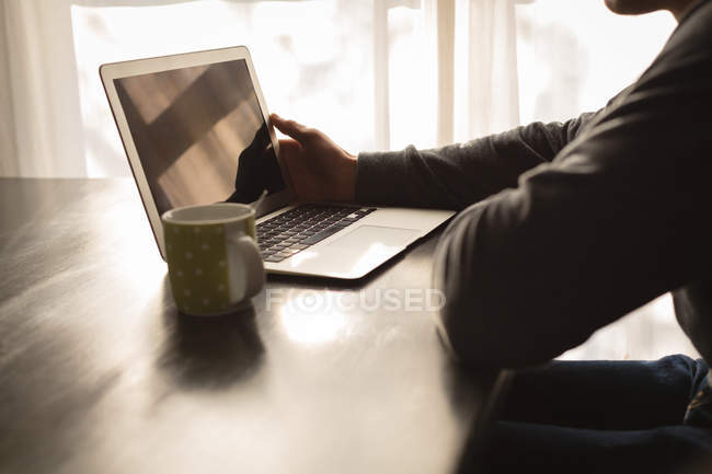 Средняя секция человека, использующего ноутбук на обеденном столе дома — стоковое фото