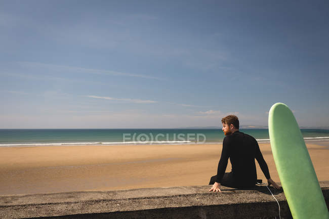 Side view of surfer with surfboard sitting on surrounding wall — Stock Photo