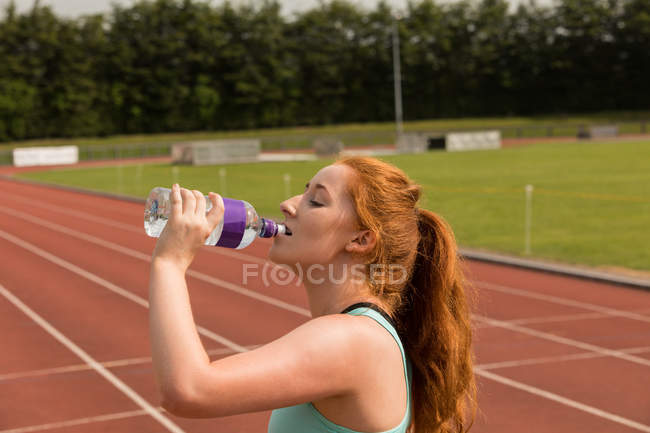 Joven mujer atlética agua potable en pista de atletismo - foto de stock