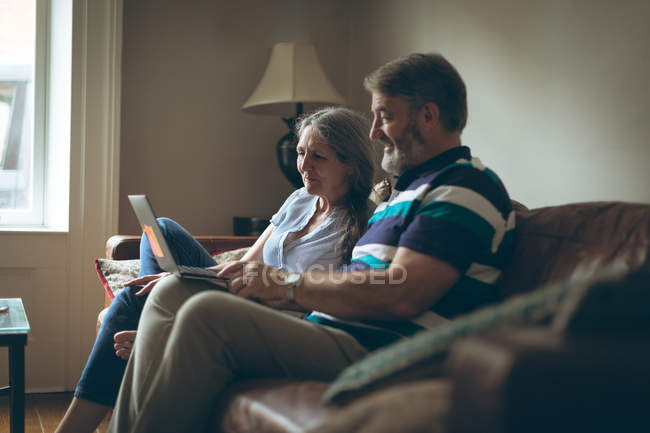 Casal sênior usando laptop na sala de estar em casa — Fotografia de Stock