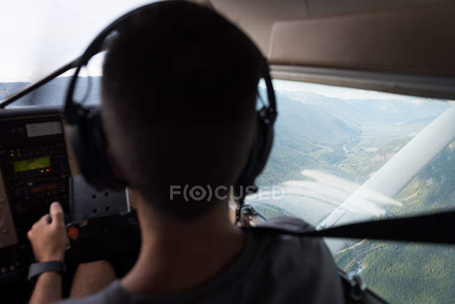 Rear view pilot flying aircraft over mountains and landscape — Stock Photo