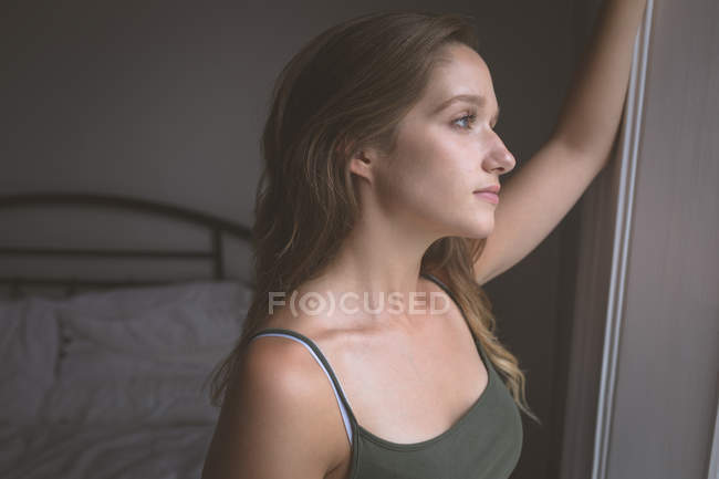 Mulher pensativa olhando através da janela em casa — Fotografia de Stock