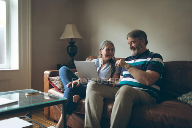 Feliz pareja de ancianos utilizando el ordenador portátil en la sala de estar en casa - foto de stock