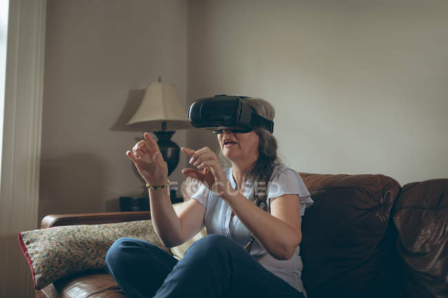 Пожилая женщина использует гарнитуру виртуальной реальности в гостиной дома — стоковое фото