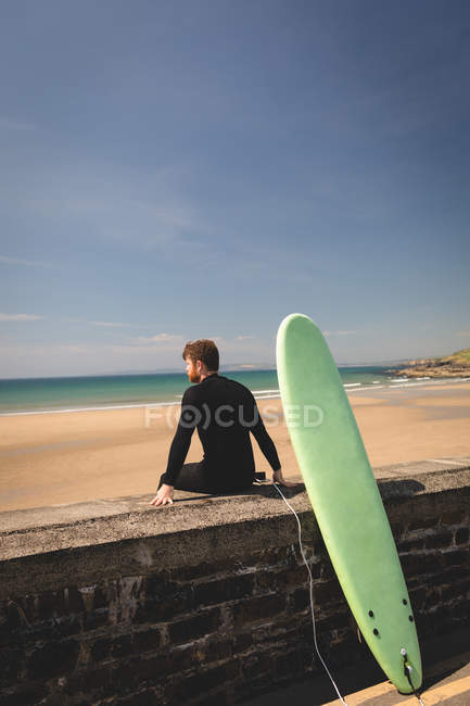 Вид збоку серфера з дошкою для серфінгу, що сидить на навколишній стіні — стокове фото