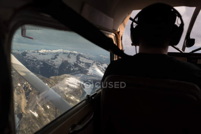 Rear view of pilot flying aircraft over snow covered mountain — Stock Photo