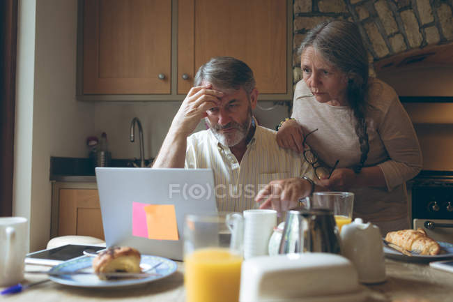 Старша пара використовує ноутбук на обідньому столі вдома — стокове фото