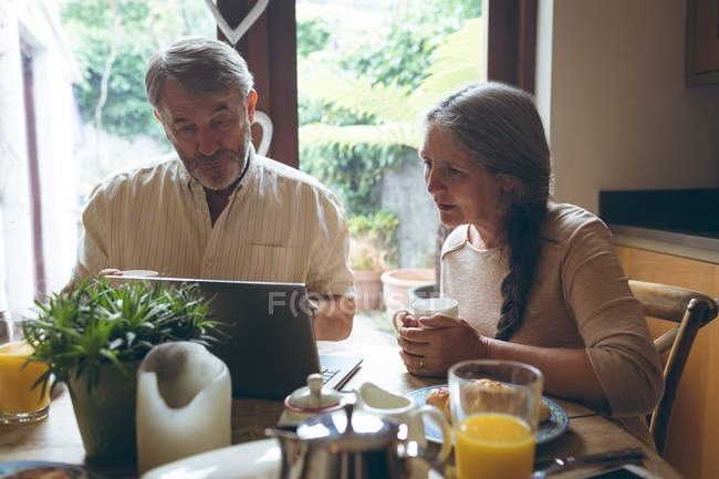 Старша пара використовує ноутбук, маючи каву вдома — стокове фото