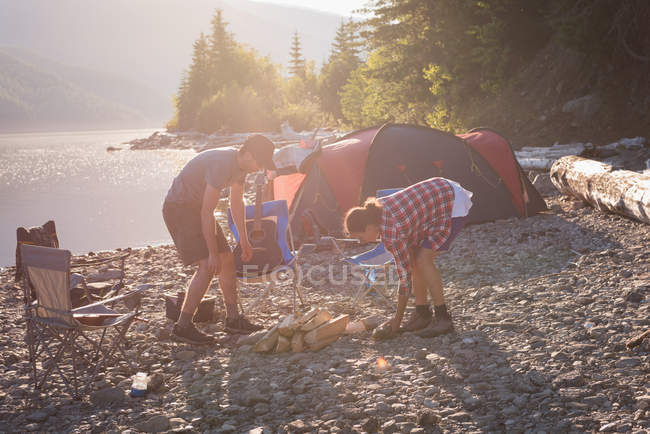 Couple préparant feu de camp près de la rivière — Photo de stock