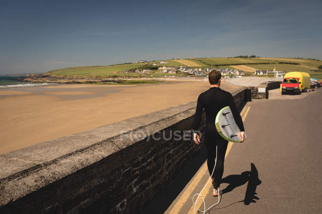 Vista posteriore del surfista con tavola da surf che cammina su strada — Foto stock