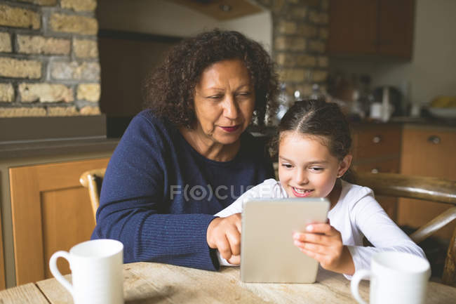 Бабушка и внучка используют цифровой планшет на кухне дома — стоковое фото