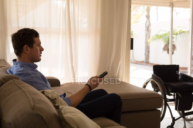 Disabled man changing channels in living room at home — Stock Photo