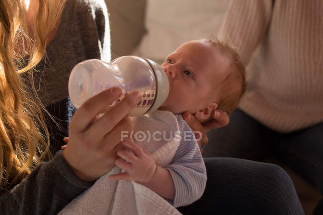 Close-up of mother feeding milk to baby on sofa at home — Stock Photo
