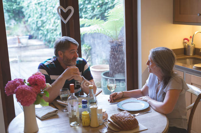 Casal sênior interagindo uns com os outros na mesa de jantar em casa — Fotografia de Stock