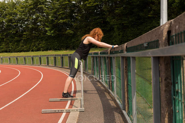 Young female athlete exercising on railing at sports track — Stock Photo