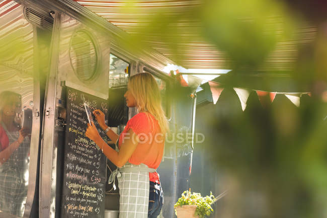 Side view of female waitress writing menu on menu board — Stock Photo