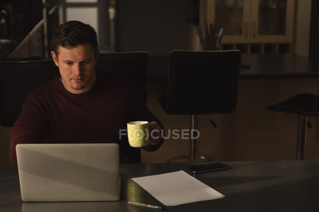 Homem tendo café ao usar laptop na mesa de jantar em casa — Fotografia de Stock