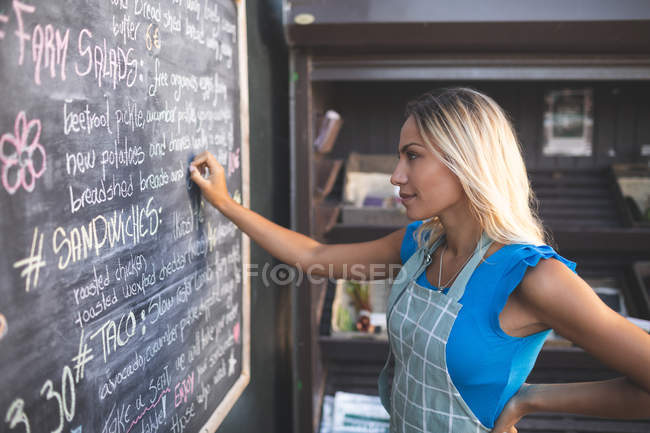 Camarera femenina escribiendo orden en el tablero de menú en camión de comida - foto de stock