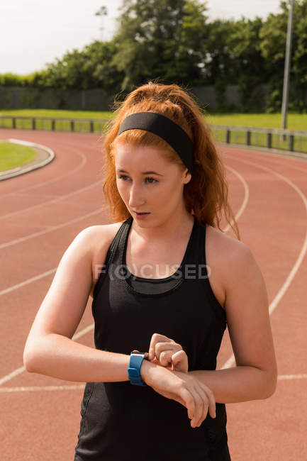 Jeune athlète féminine utilisant smartwatch sur piste de course — Photo de stock