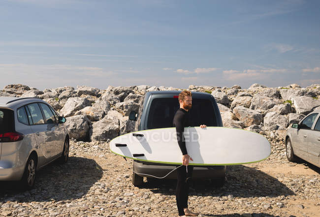 Surfista segurando prancha de surf perto da praia em um dia ensolarado — Fotografia de Stock