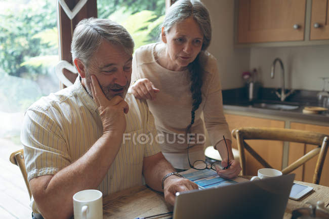 Seniorenpaar benutzt Laptop auf Esstisch zu Hause — Stockfoto