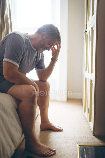 Homme âgé tendu assis sur le lit dans la chambre à coucher à la maison — Photo de stock