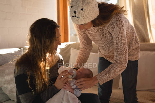 Mother feeding milk to baby on sofa at home — Stock Photo