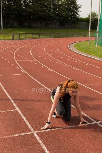 Jeune athlète féminine prête à courir sur piste de course — Photo de stock
