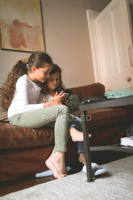 Girls using mobile phone on sofa at home — Stock Photo