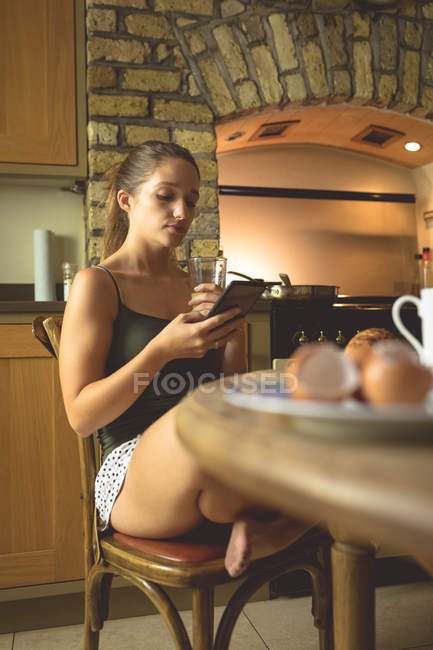 Mujer usando teléfono móvil en la mesa de comedor en casa - foto de stock