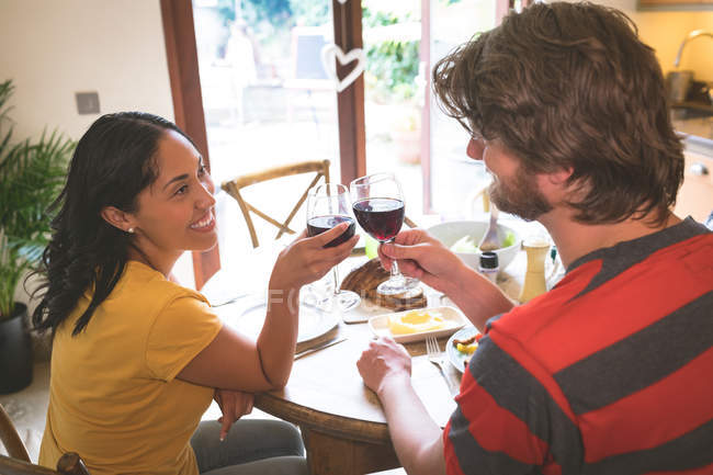 Casal tendo vinho tinto na mesa de jantar em casa — Fotografia de Stock