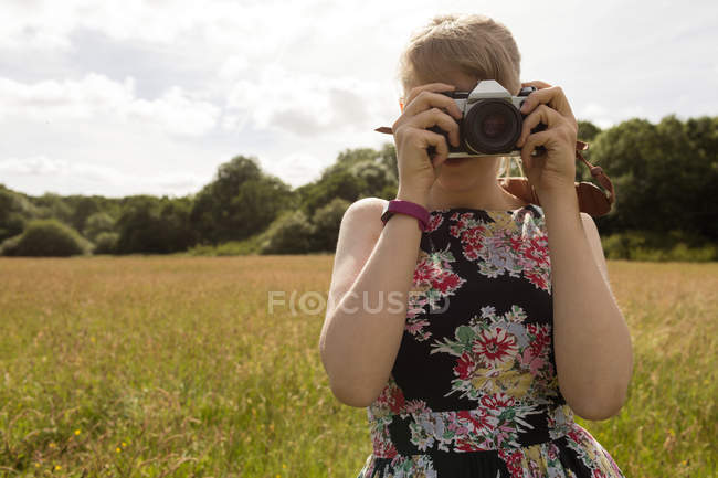 Mujer haciendo clic en la foto con cámara digital en el campo - foto de stock