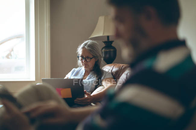 Mujer mayor usando el ordenador portátil en la sala de estar en casa - foto de stock