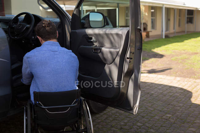 Вид сзади инвалида в инвалидной коляске возле автомобиля — стоковое фото
